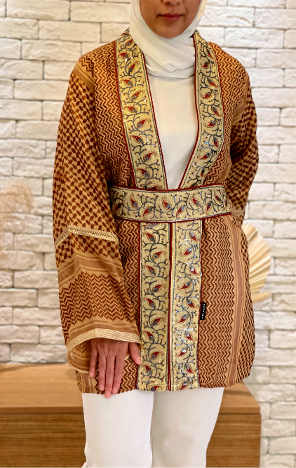 Model wearing the Kayi Keffiyeh Kimono belted over a white outfit — olive and gold ghutrah weave