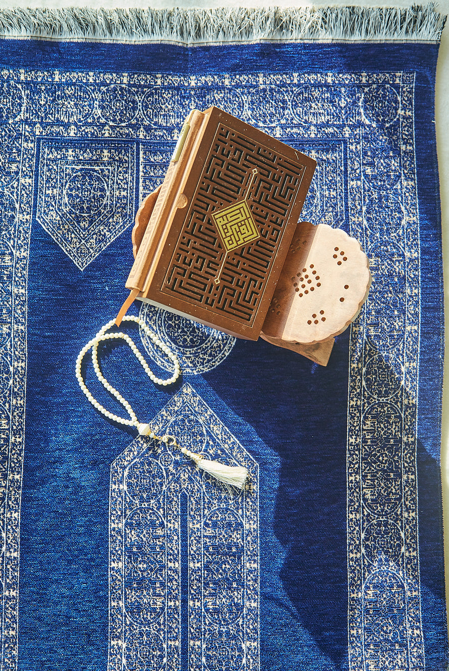 Blue Mecca Collection prayer mat styled with Quran and white prayer beads