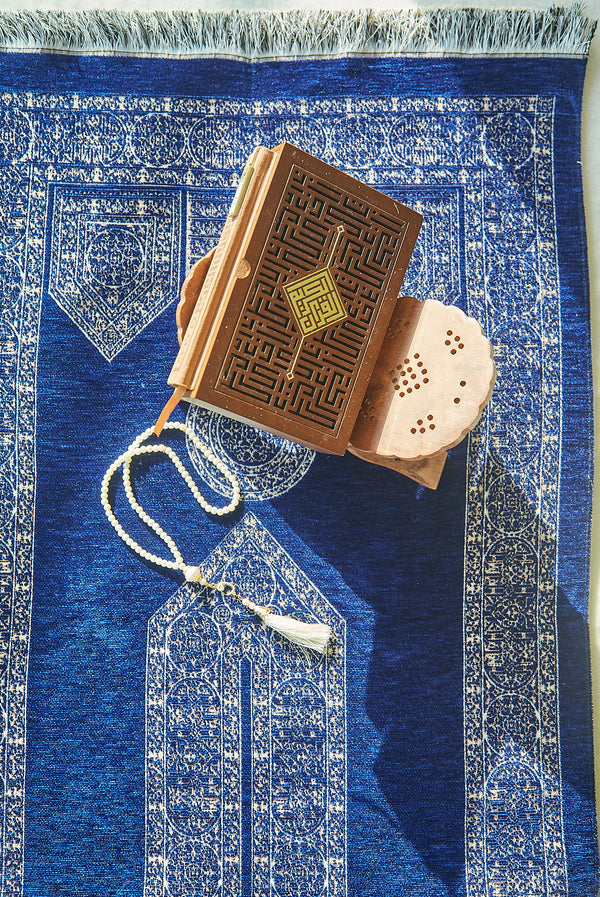 Blue Mecca Collection prayer mat styled with Quran and white prayer beads