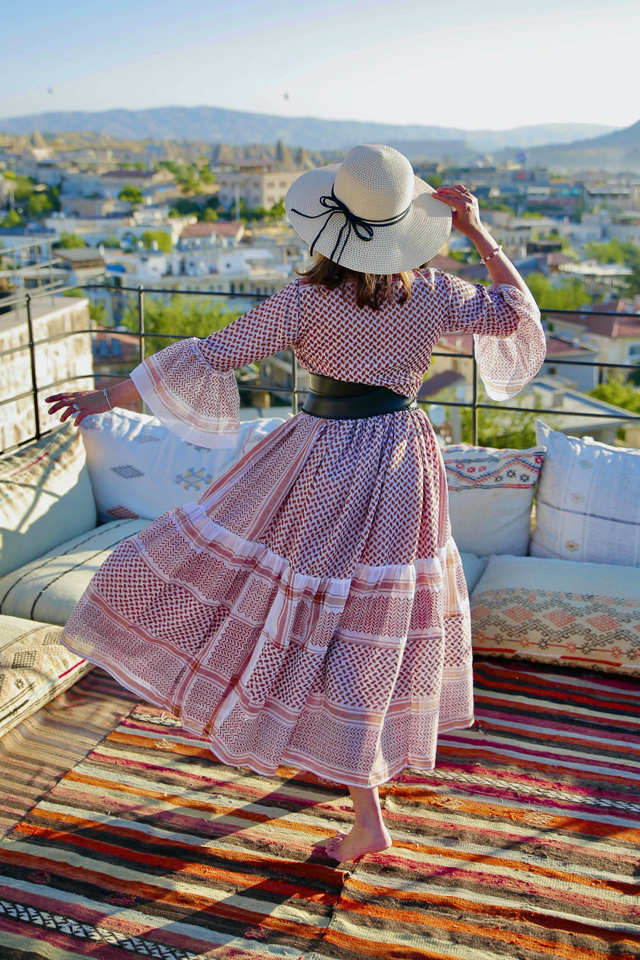 Woman in a pink keffiyeh dress and hat on a rooftop with a cityscape view