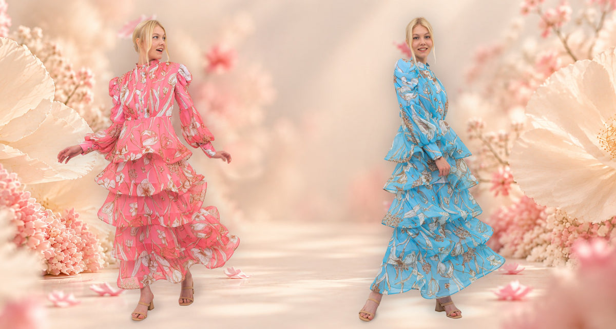 The Bloom Edit tiered floral dresses in Coral Pink and Azure Blue against a soft floral backdrop.
